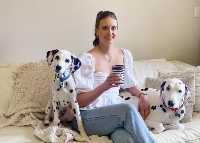 A photo of a weight loss nutritionist and personal trainer holding a coffee cup, accompanied by her two dogs, symbolising a relaxing break during the coaching session.
